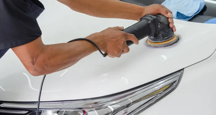 A detailer running a dual-action polisher across a car bonnet
