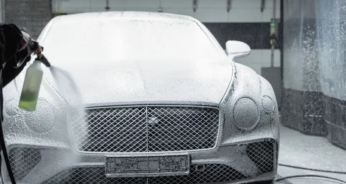 A car covered in thick snow foam during a wash inside a detailing garage