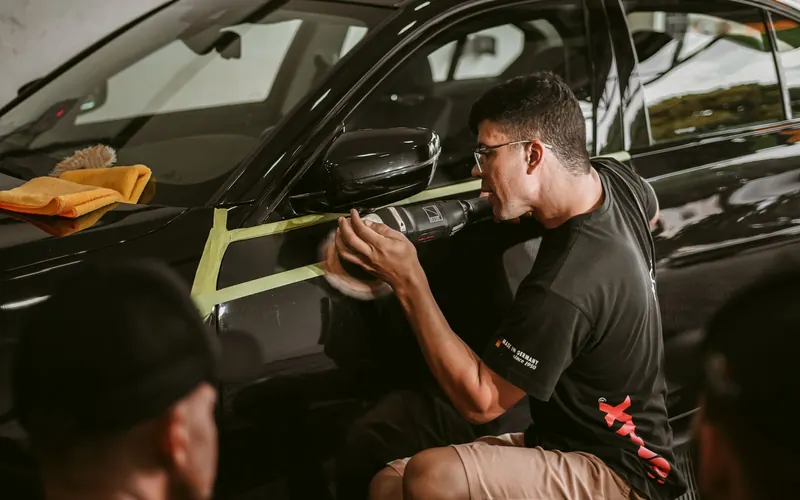 A detailer working along the panel of a black car during a correction job