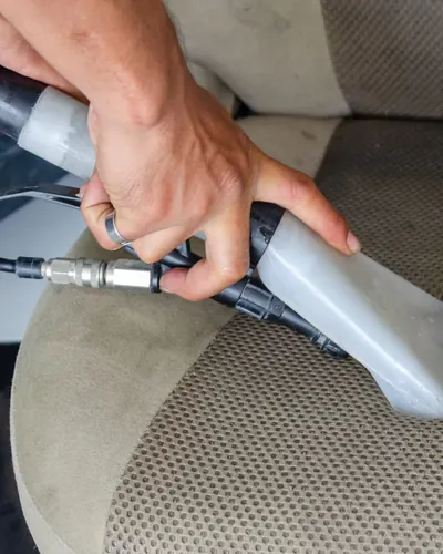 A vacuum nozzle deep-cleaning a fabric car seat
